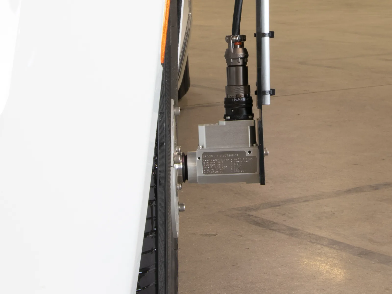 Seitenansicht eines Raddrehzahlsensors auf seiner Spannplatte, mit dem Stecker und der an der Hülse befestigten Haltestange des Stators